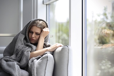 Photo of Depressed young woman sitting on sofa at home