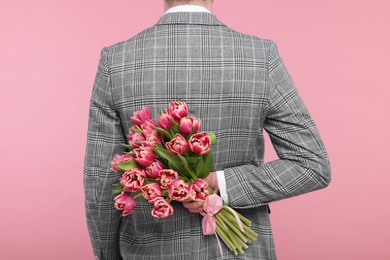 Man hiding beautiful bouquet on pink background, back view