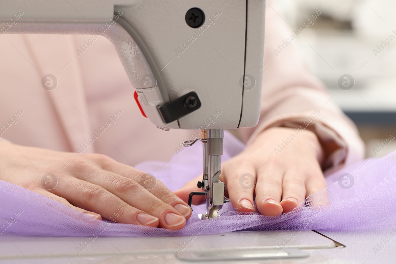 Photo of Dressmaker sewing new dress with machine in atelier, closeup