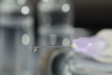 Photo of Drop of medication on syringe needle against blurred background, closeup. Space for text