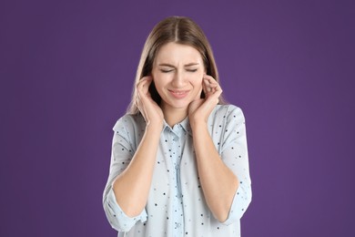 Photo of Emotional young woman covering her ears with fingers on purple background