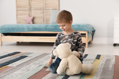 Photo of Cute little boy playing with teddy bear at home