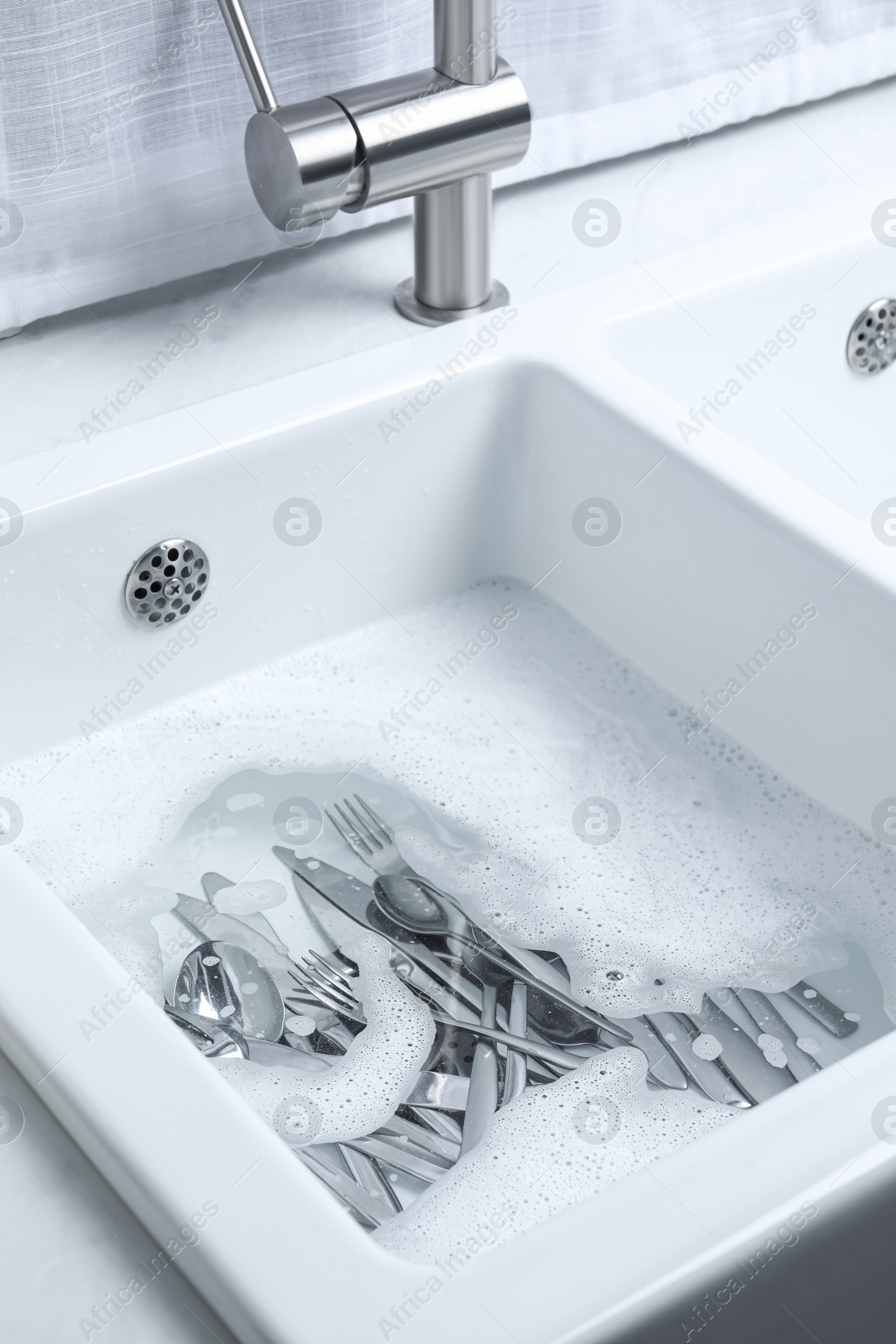 Photo of Washing silver spoons, forks and knives in kitchen sink with foam, above view