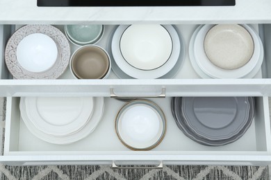 Open drawers with different plates and bowls in kitchen, top view