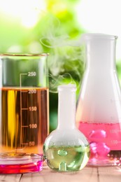 Laboratory glassware with colorful liquids on wooden table outdoors. Chemical reaction