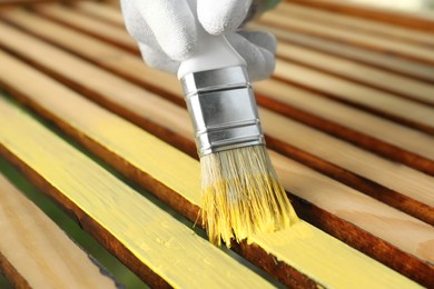 Photo of Woman painting wooden surface with yellow dye, closeup