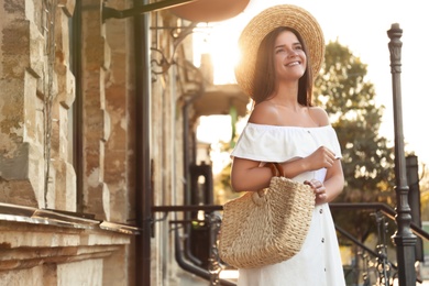 Photo of Young woman with stylish straw bag outdoors. Space for text