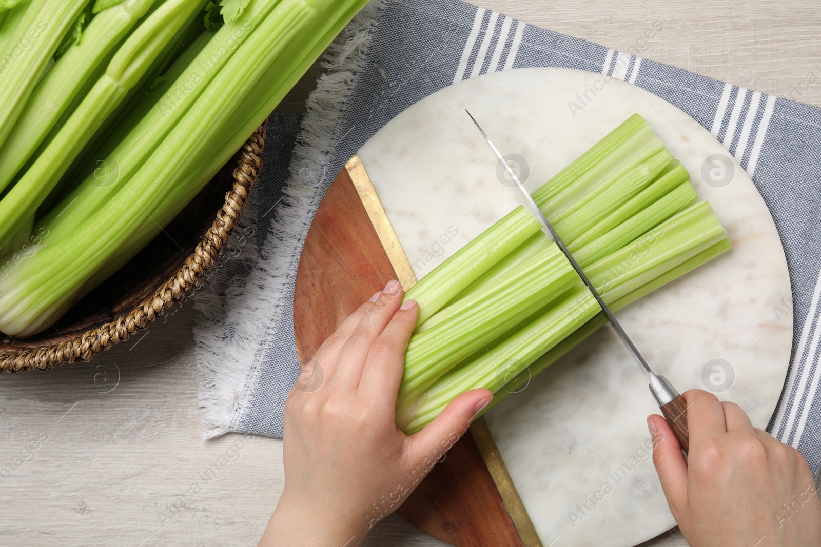Photo of Woman cutting fresh green celery at white wooden table, top view