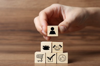 Professional buyer. Woman building pyramid of cubes with different icons on wooden background, closeup