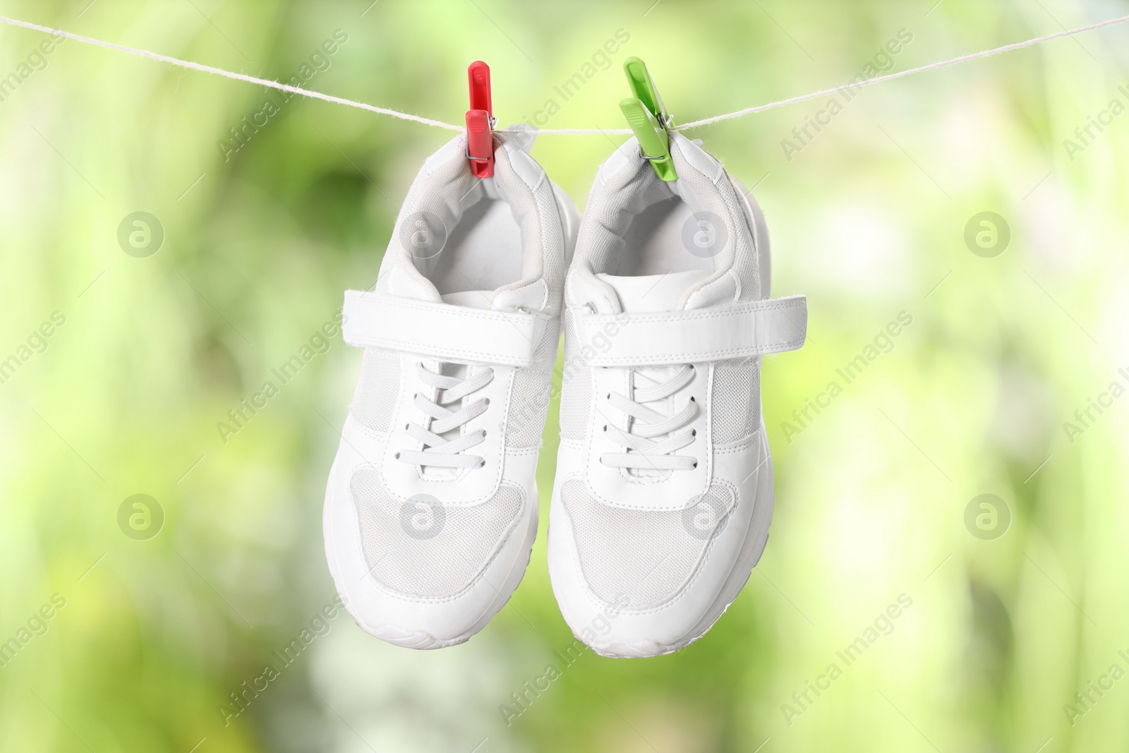 Photo of Stylish sneakers drying on washing line against blurred background