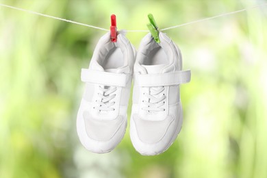 Photo of Stylish sneakers drying on washing line against blurred background