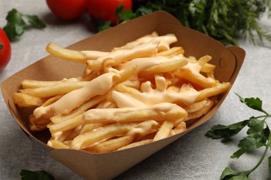 Photo of Tasty potato fries, cheese sauce in paper container and products on grey table, closeup