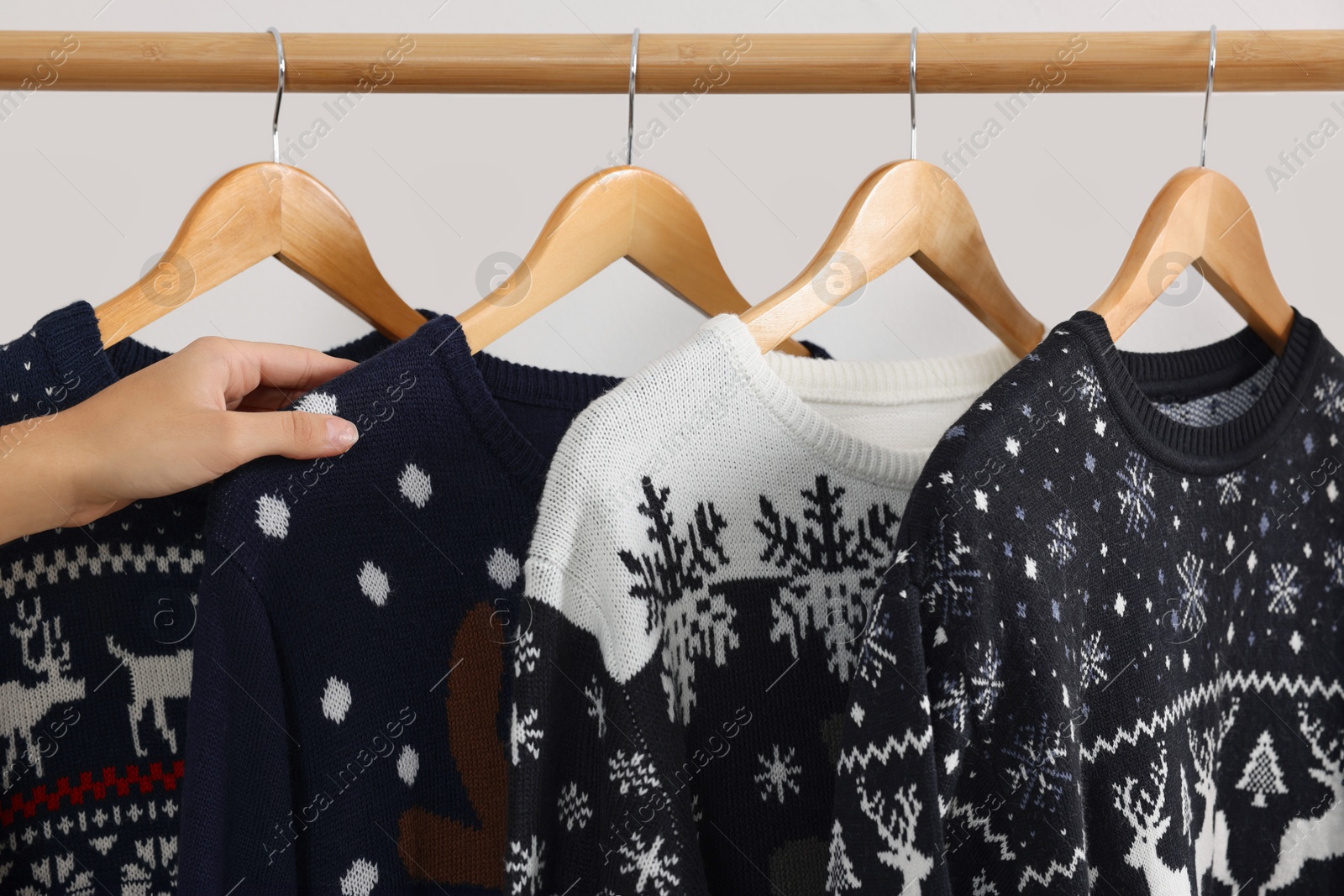 Photo of Woman choosing Christmas sweater from rack near white wall, closeup