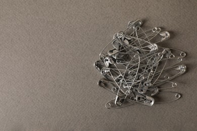 Photo of Pile of safety pins on grey textured background, flat lay. Space for text