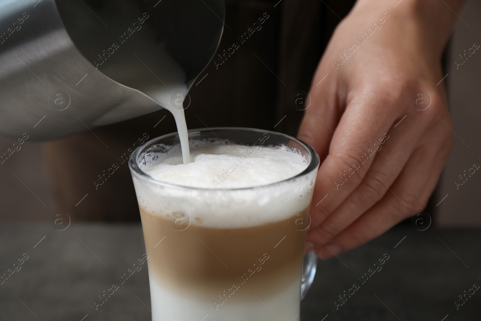 Photo of Woman pouring milk into cup of coffee at grey table, closeup