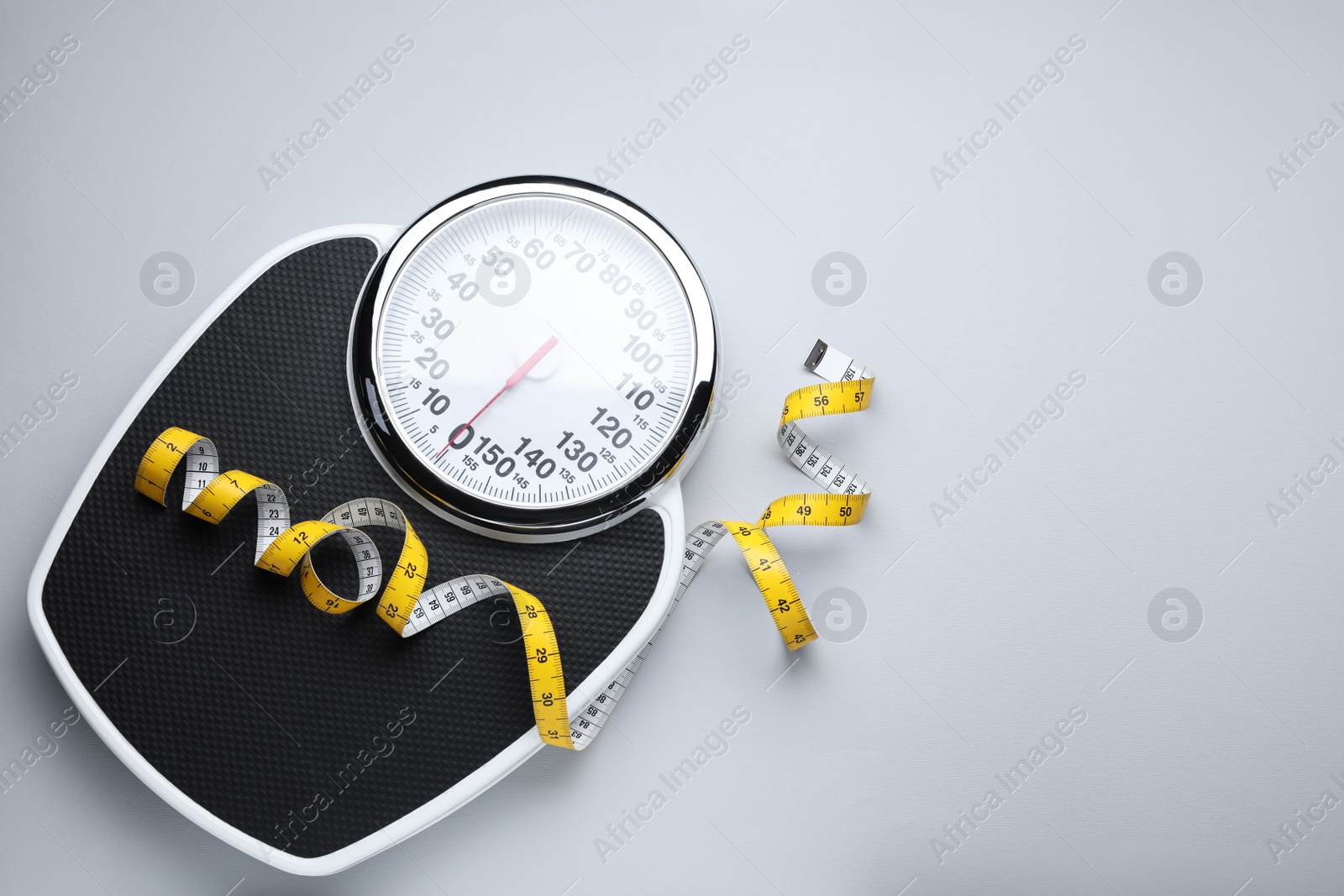 Photo of Scales and measuring tape on light grey background, top view. Space for text