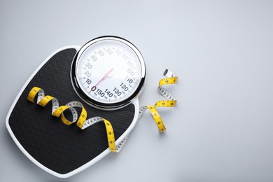 Photo of Scales and measuring tape on light grey background, top view. Space for text