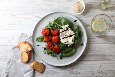Delicious burrata cheese served with tomatoes, croutons, arugula and basil on white wooden table, flat lay