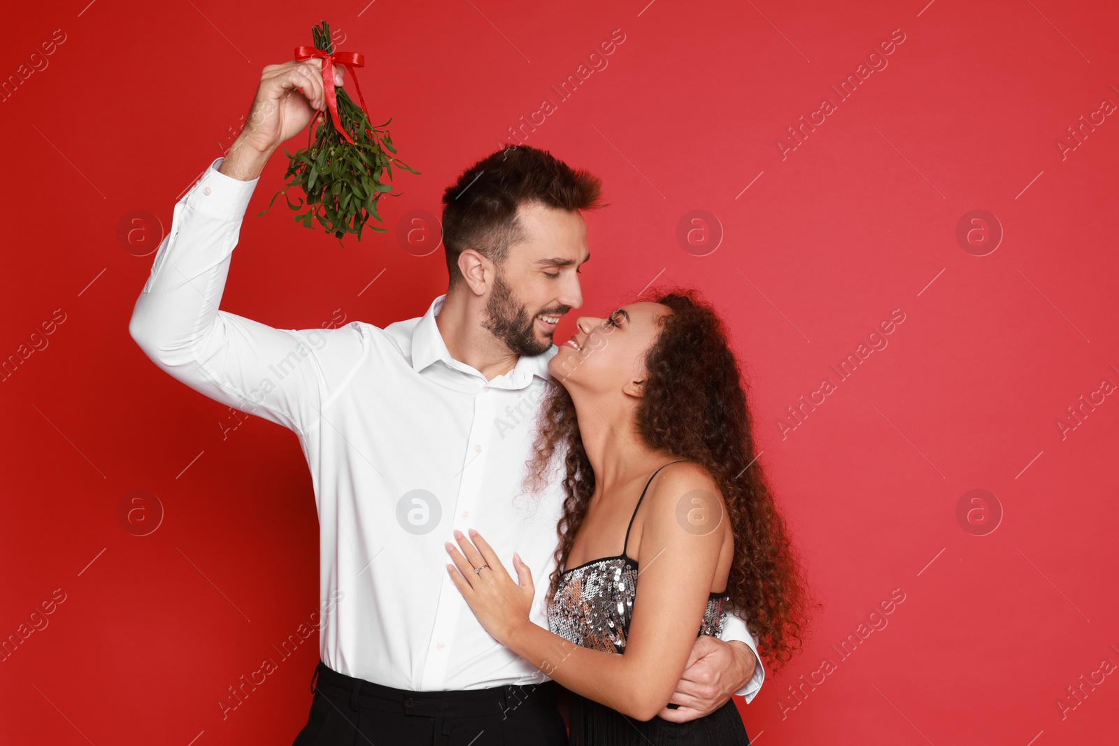 Photo of Lovely couple under mistletoe bunch on red background