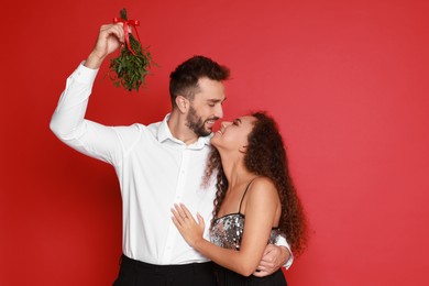 Lovely couple under mistletoe bunch on red background