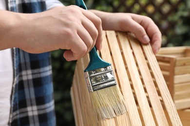 Photo of Man applying varnish onto wooden crate against blurred background, closeup
