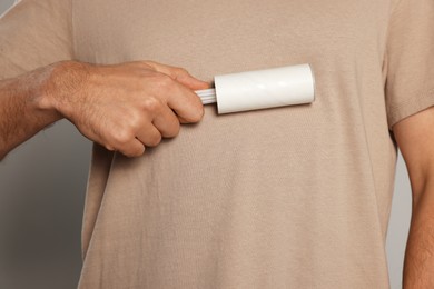 Man using lint roller on light grey background, closeup