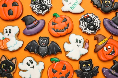 Different decorated gingerbread cookies on orange background, flat lay. Halloween celebration