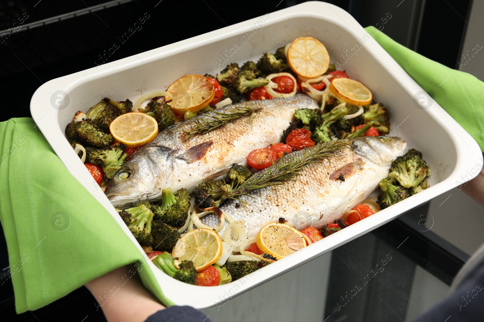 Photo of Woman taking baking dish with delicious fish and vegetables from oven, closeup