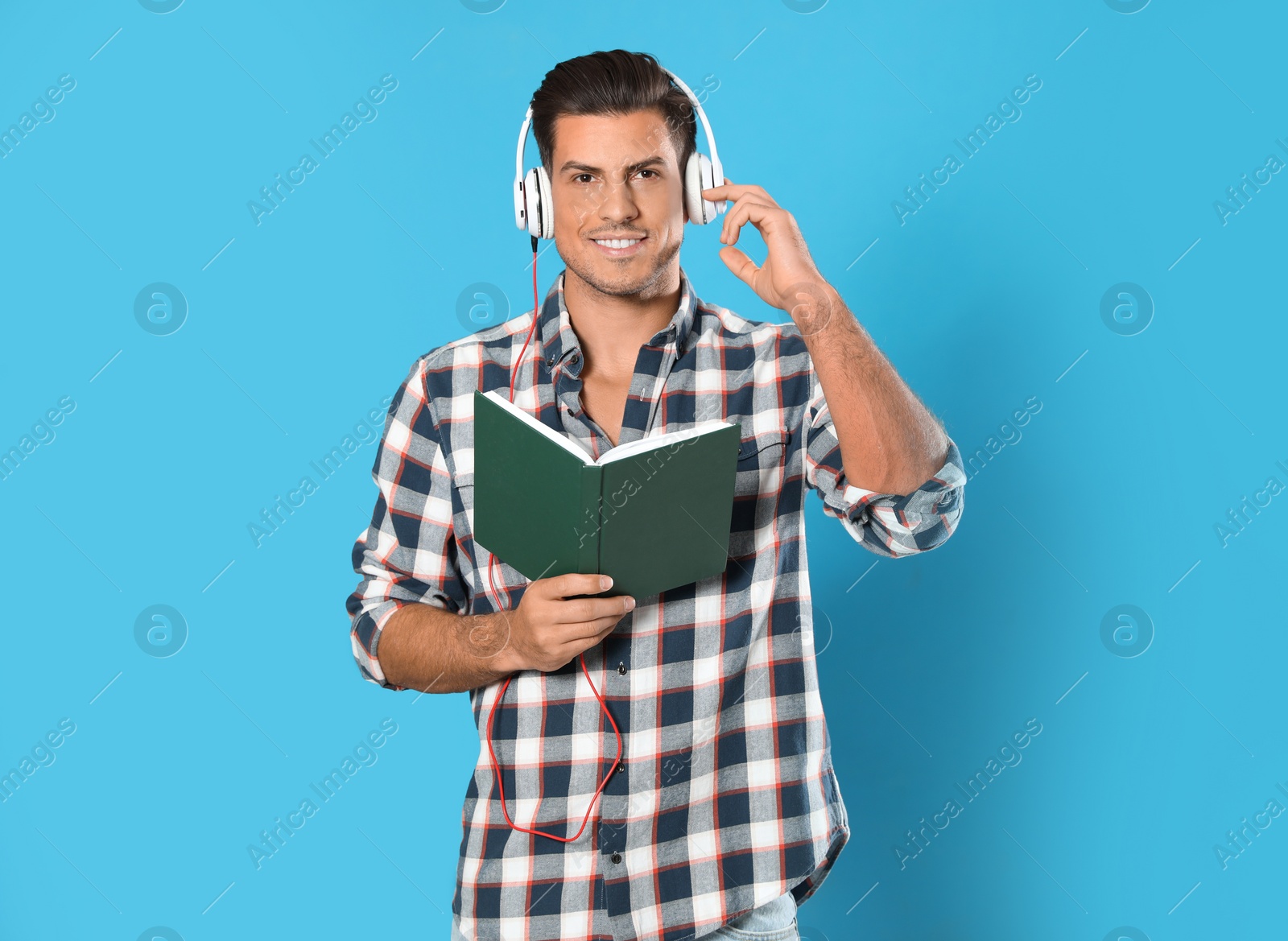 Photo of Man with headphones and book on light blue background. Audiobook concept