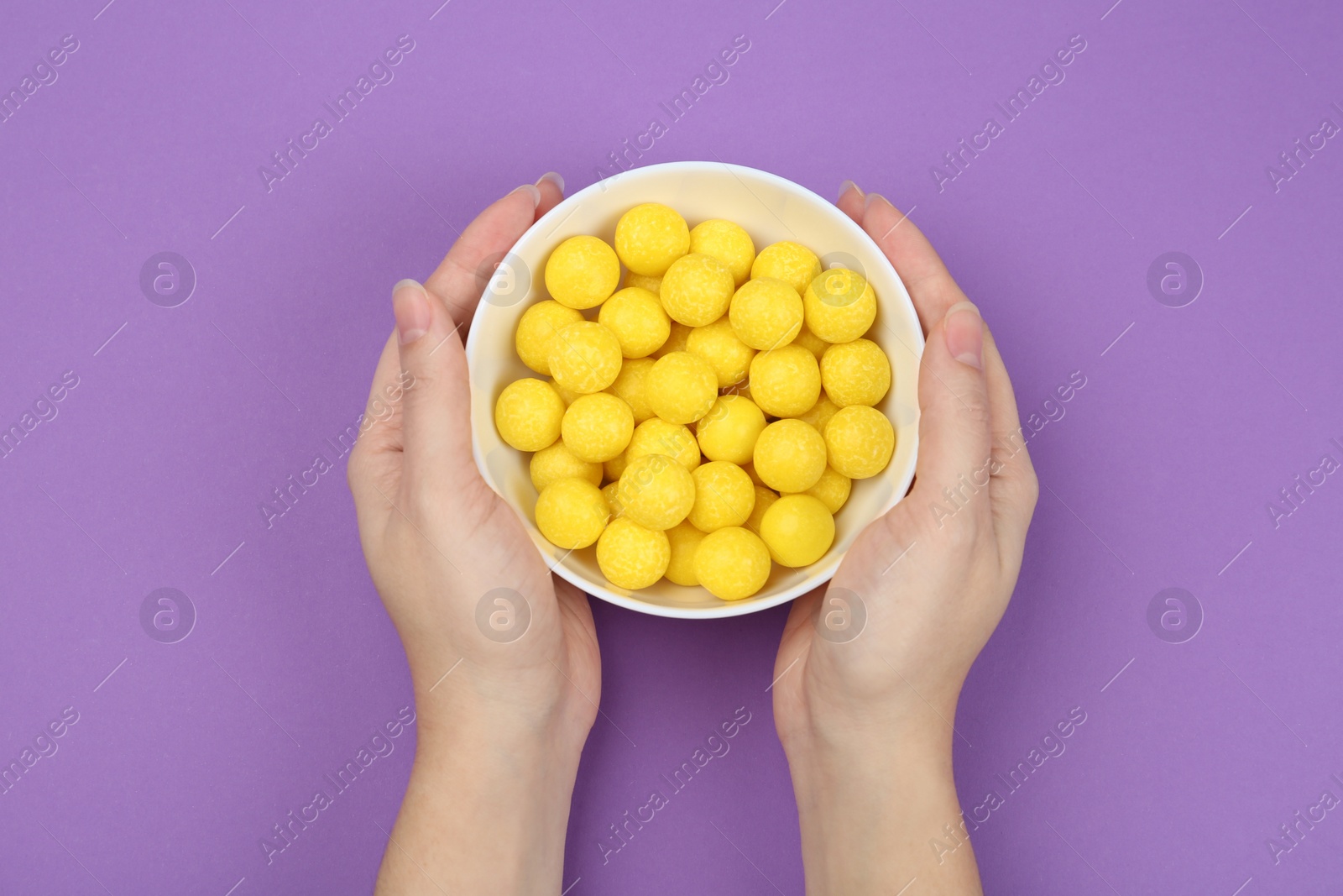 Photo of Woman holding bowl of lemon drops on purple background, top view