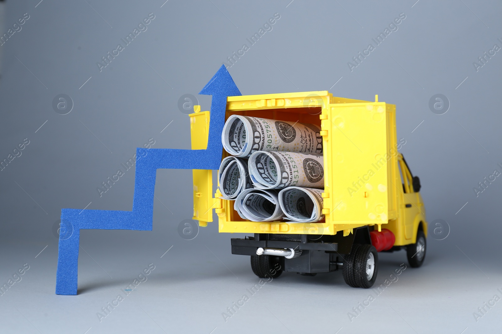 Photo of Economic profit. Arrow and toy truck with banknotes on light grey background