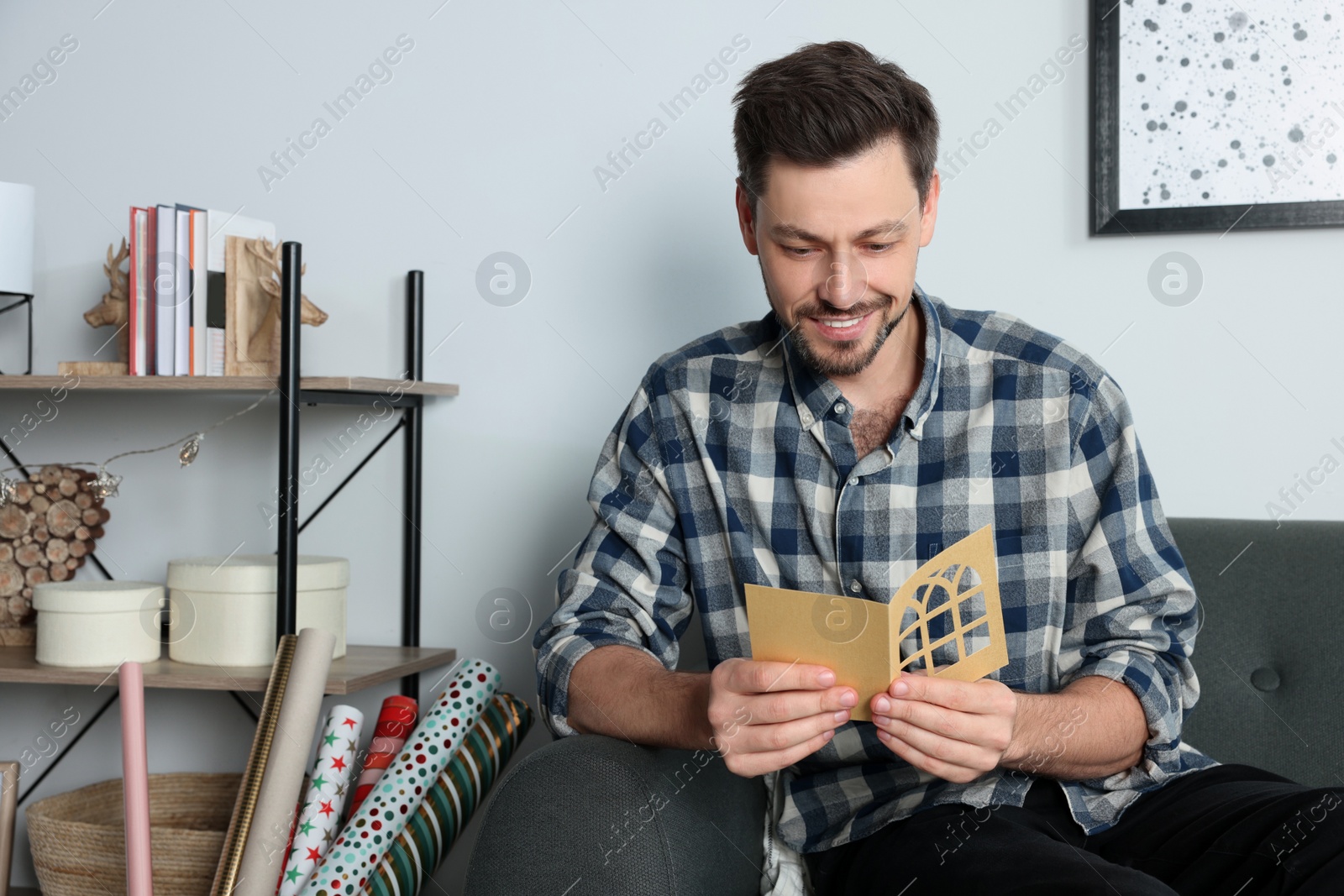 Photo of Happy man reading greeting card on sofa in living room