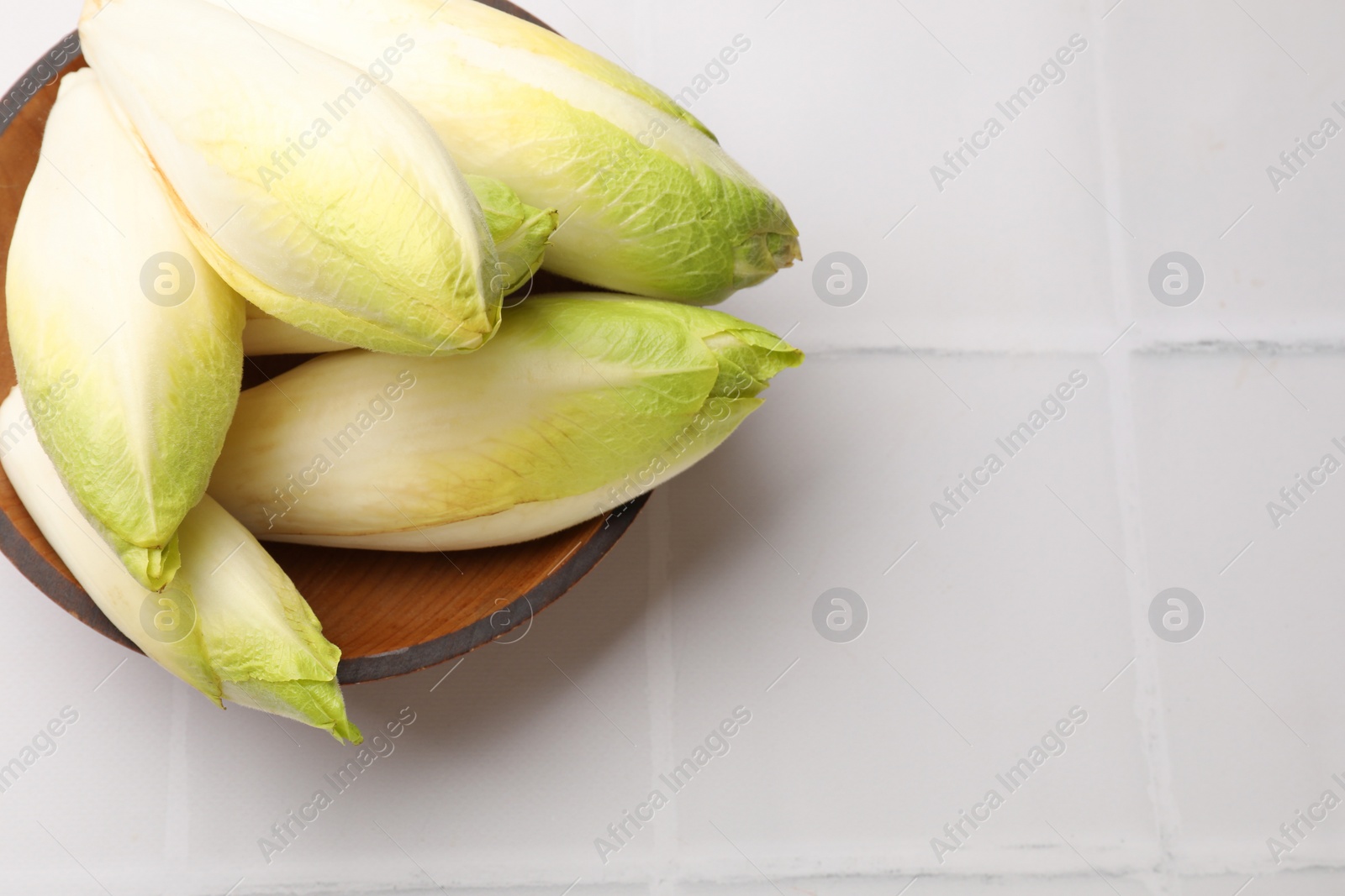 Photo of Fresh raw Belgian endives (chicory) in bowl on white tiled table, top view. Space for text