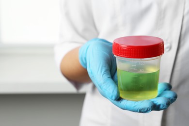 Photo of Doctor holding container with urine sample for analysis indoors, closeup