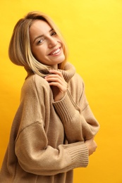 Beautiful young woman wearing knitted sweater on yellow background