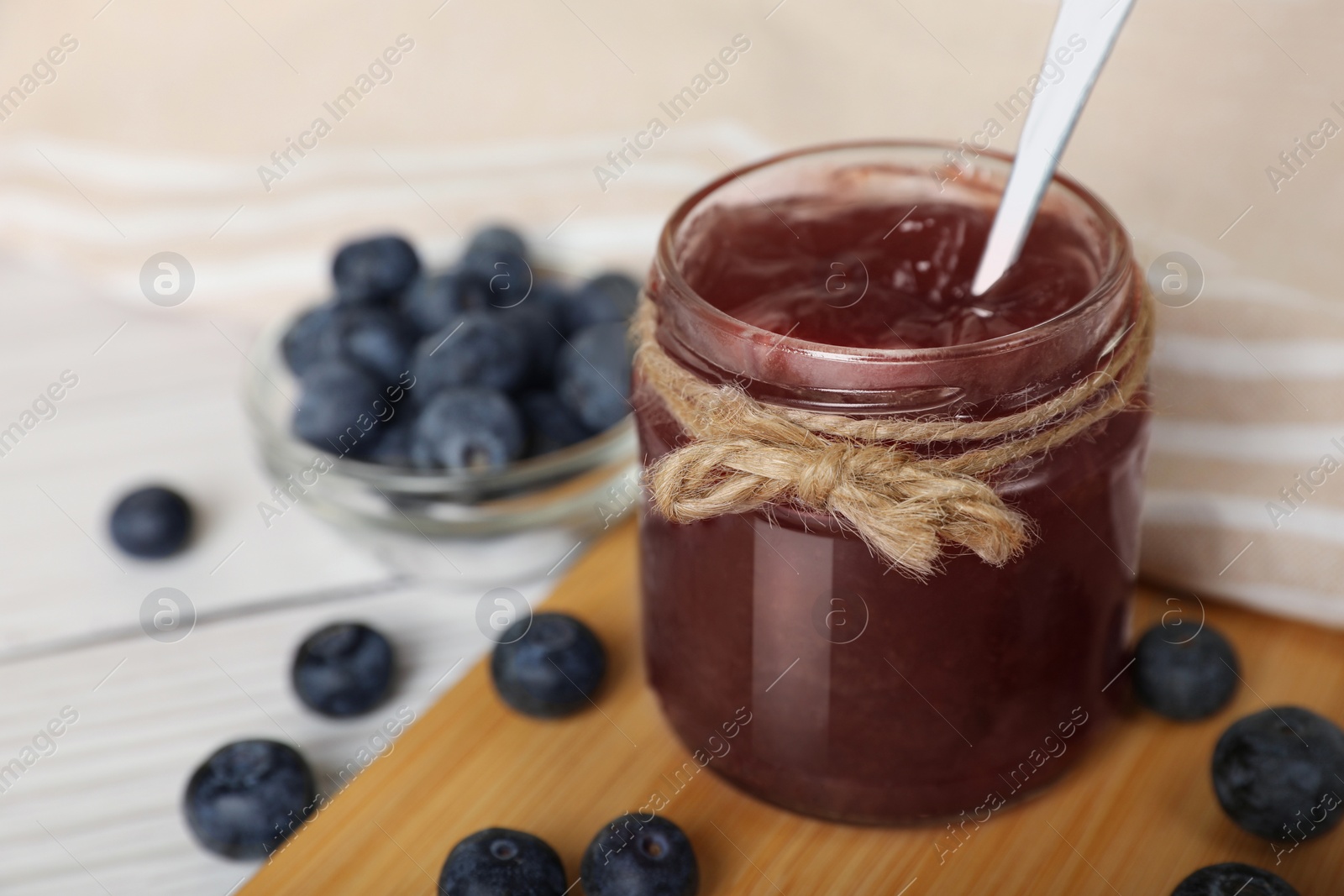 Photo of Jar of delicious blueberry jam and fresh berries on white table, closeup. Space for text