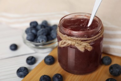 Photo of Jar of delicious blueberry jam and fresh berries on white table, closeup. Space for text