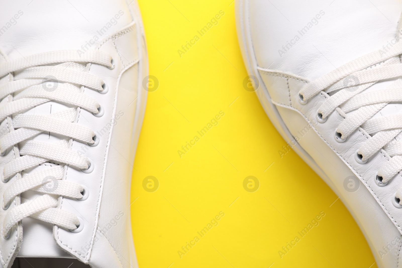 Photo of Pair of stylish white sneakers on yellow background, top view