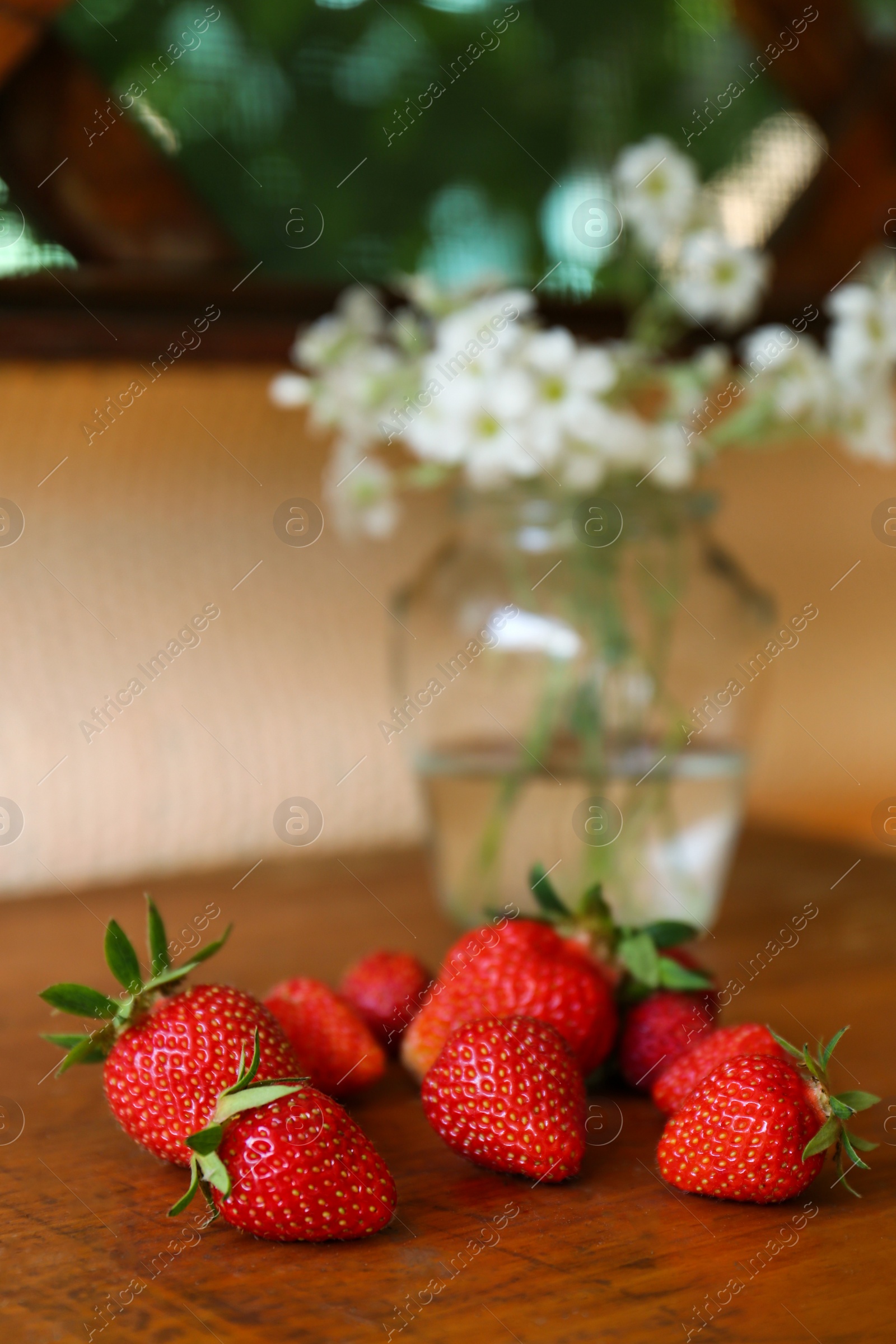 Photo of Fresh ripe strawberries and bouquet of beautiful flowers on wooden table, closeup