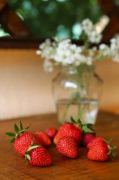 Photo of Fresh ripe strawberries and bouquet of beautiful flowers on wooden table, closeup