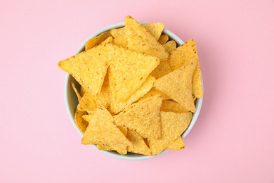 Photo of Bowl with tasty Mexican nachos chips on pink background, top view