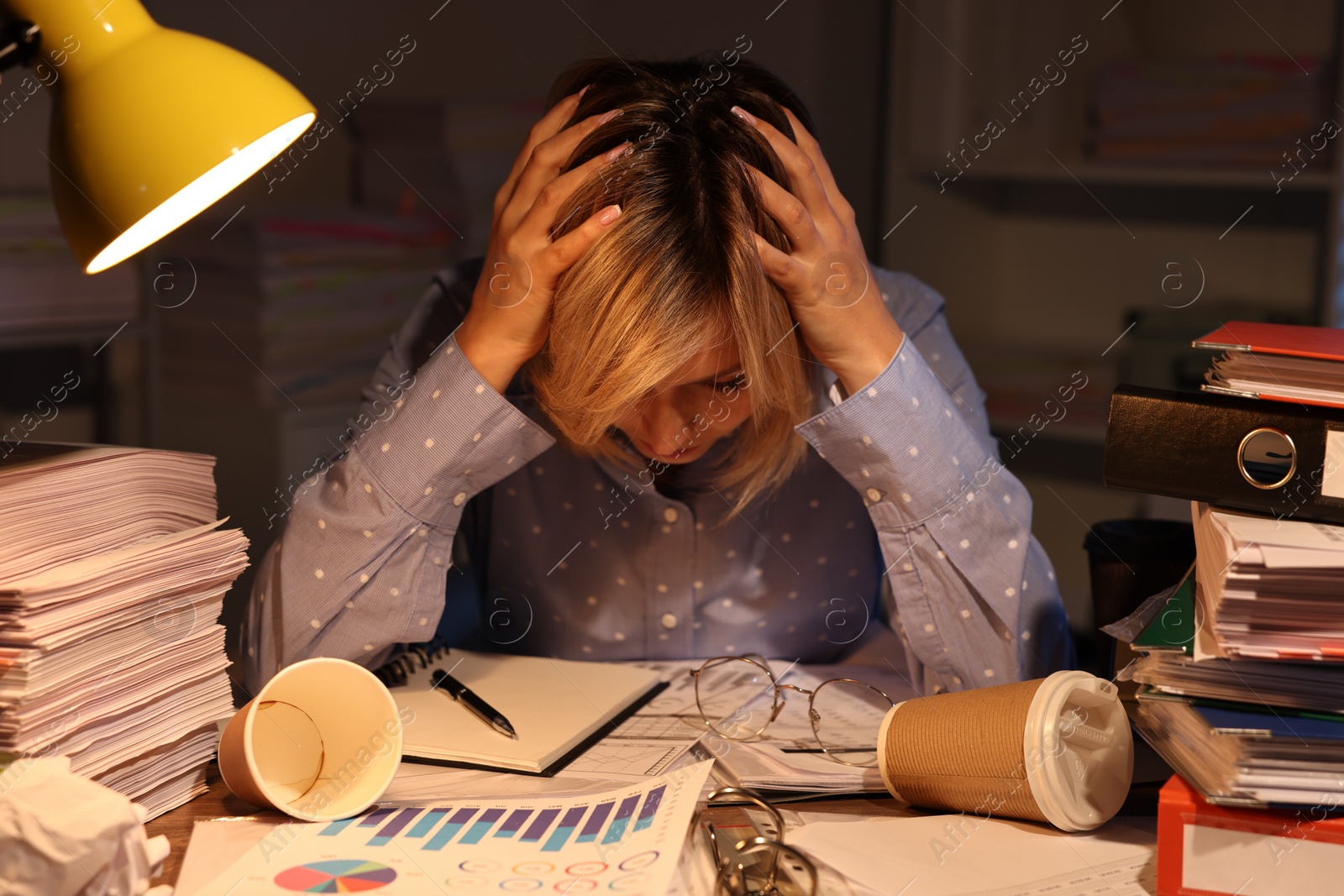Photo of Overwhelmed woman surrounded by documents and paper coffee cups at table in office at night