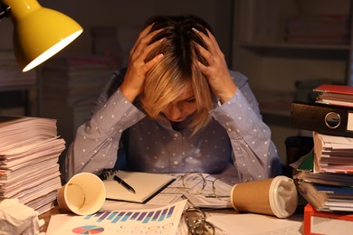 Overwhelmed woman surrounded by documents and paper coffee cups at table in office at night