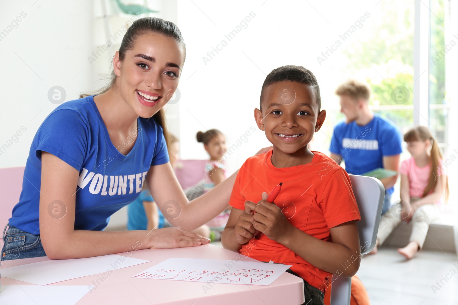 Photo of Little African-American boy learning alphabet with volunteer at table indoors