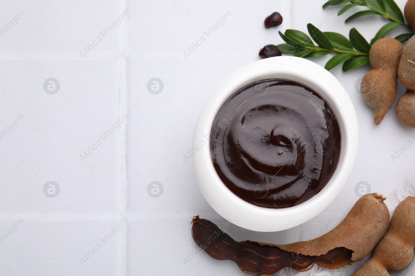 Bowl of tasty tamarind sauce, leaves and fresh pods on white tiled table, flat lay. Space for text Photo of Bowl of tasty tamarind sauce, leaves and fresh pods on white tiled table, flat lay. Space for text