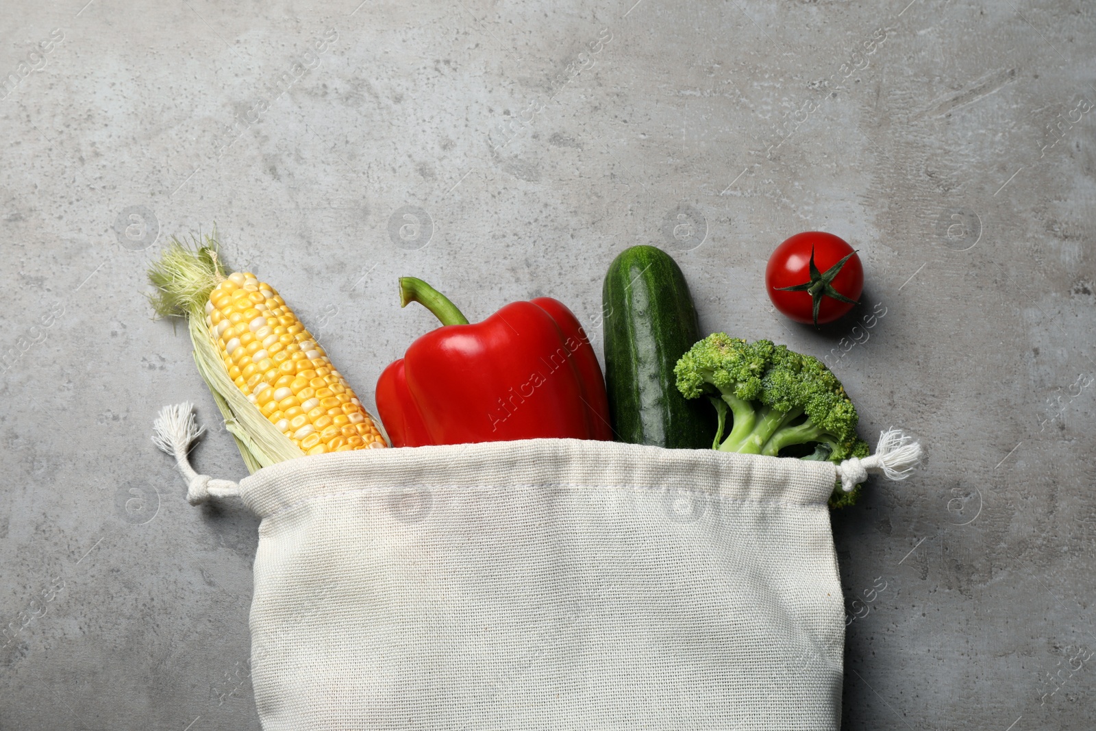 Photo of Cloth bag with different fresh vegetables on grey table, flat lay