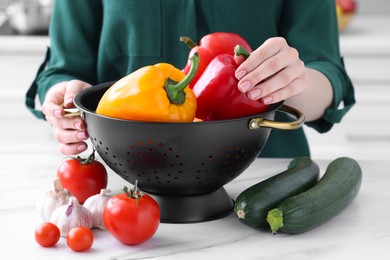 Woman holding black colander with bell pepper at white marble table indoors, closeup