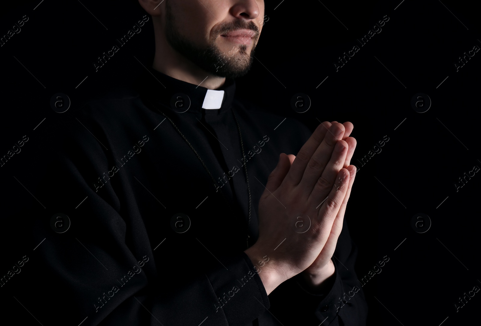 Photo of Priest in cassock praying on dark background, closeup