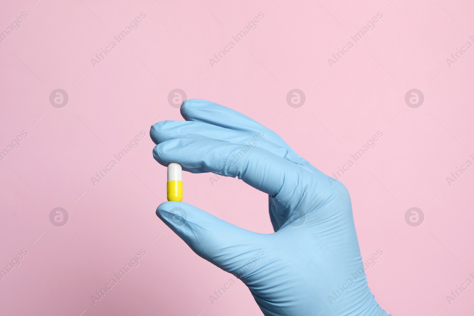 Photo of Doctor holding pill on pink background, closeup