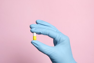 Doctor holding pill on pink background, closeup